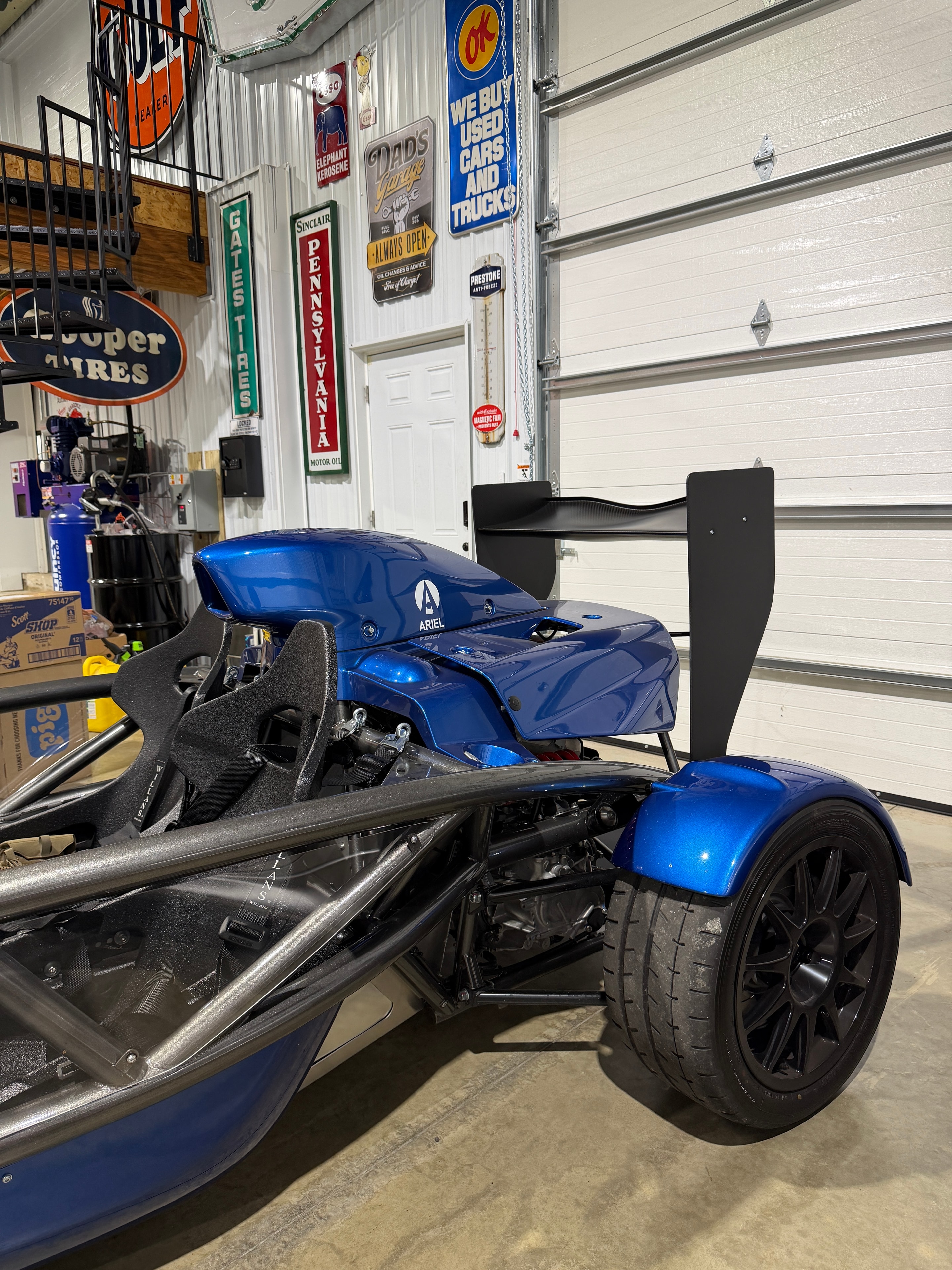 2025 Ariel Atom 4 in the SuperCar Garage shop — side view with vintage oil signs